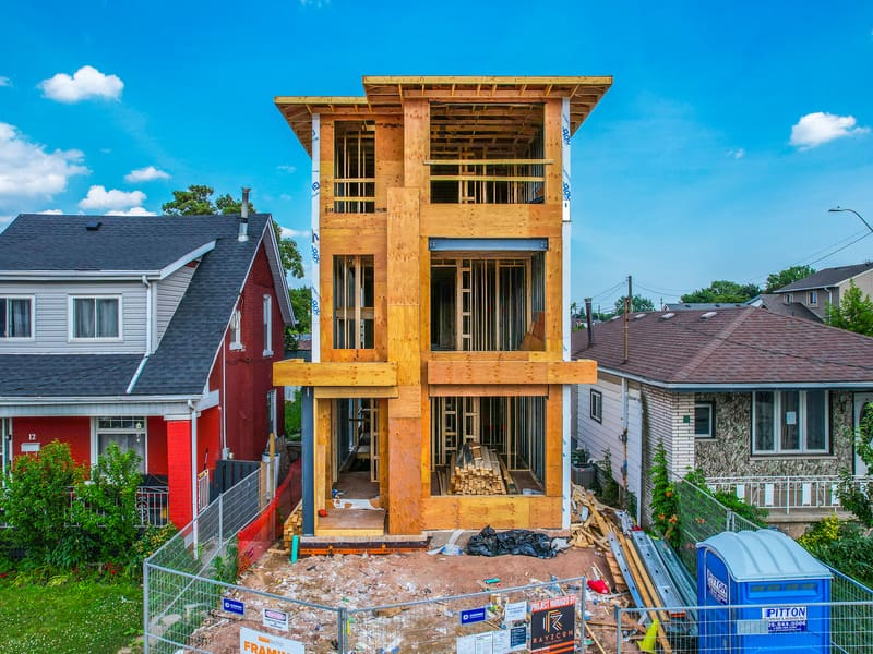 Front view of three-storey multiplex during wood framing between existing homes in Hamilton
