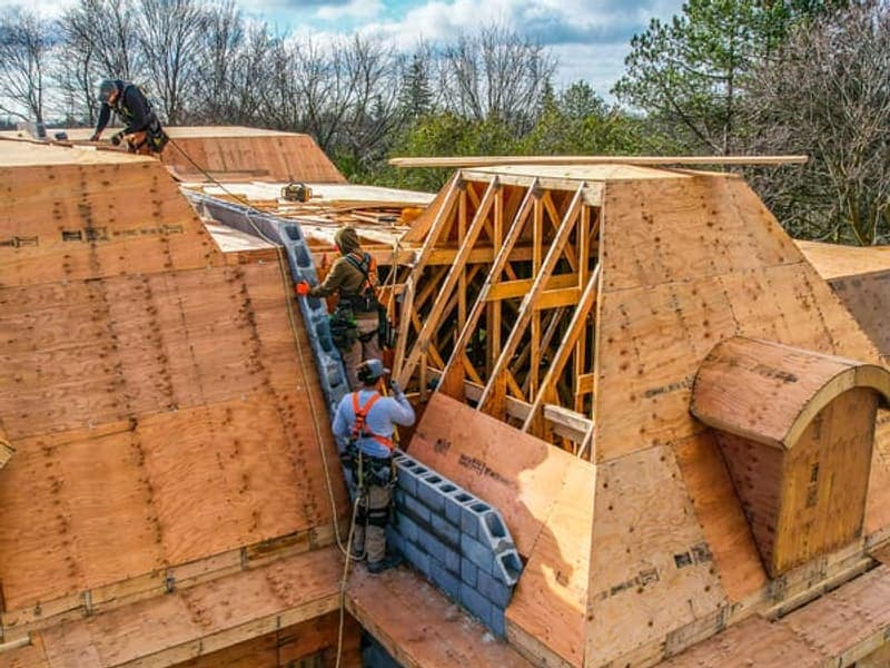 Framing crew installing roof sheathing on custom home with safety harnesses