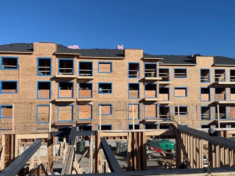 Three-storey townhouse block showing completed wood framing with OSB sheathing and blue housewrap