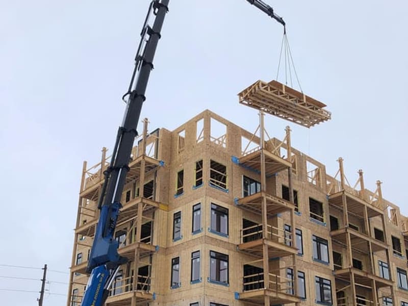 Crane lifting prefabricated roof panel onto wood-framed townhouse building in Toronto