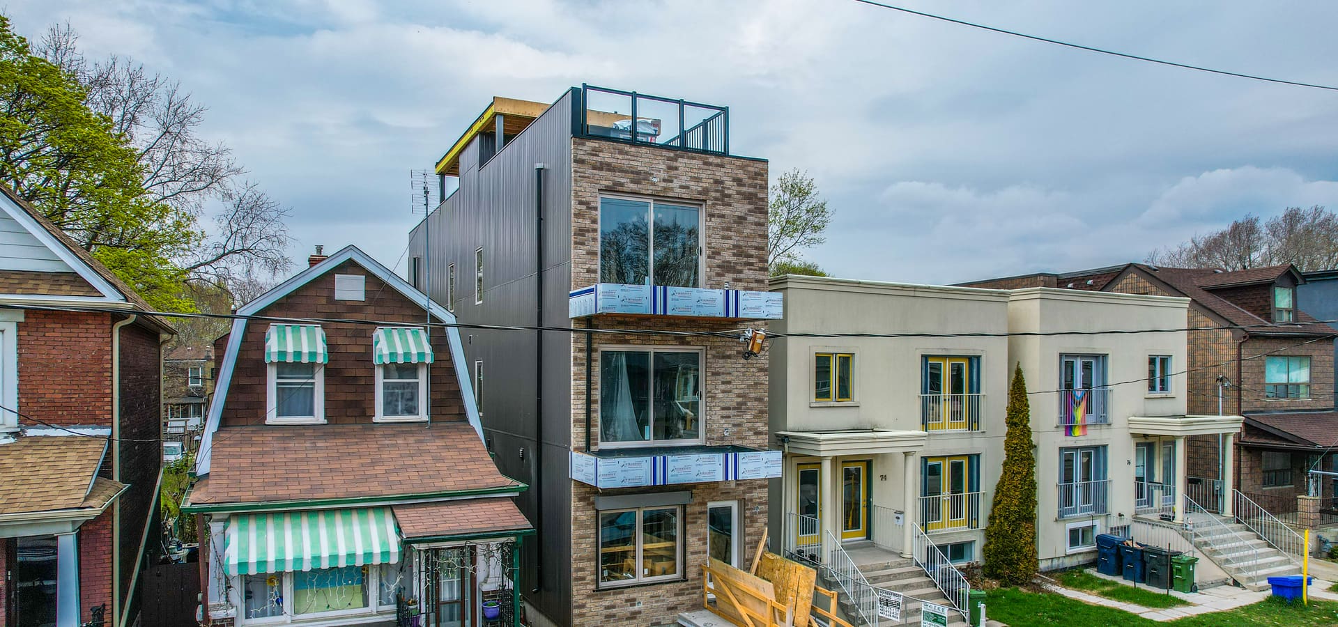 Wide view of four-storey multiplex with mixed brick and dark metal cladding in Leslieville