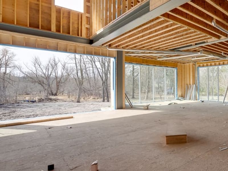 Interior open concept space with steel beams and floor-to-ceiling windows overlooking trees