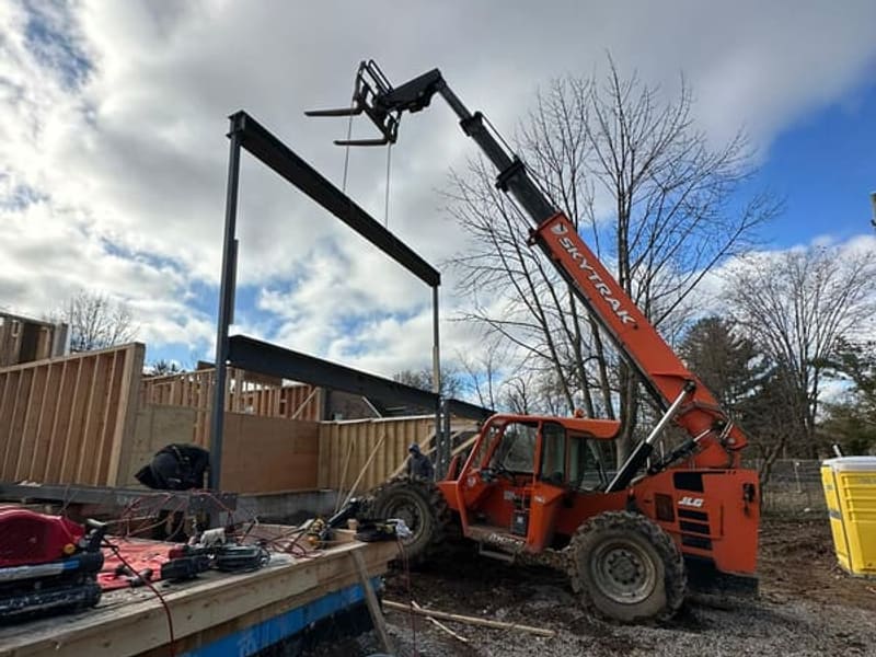 Telehandler lifting steel moment frame into place during custom home construction
