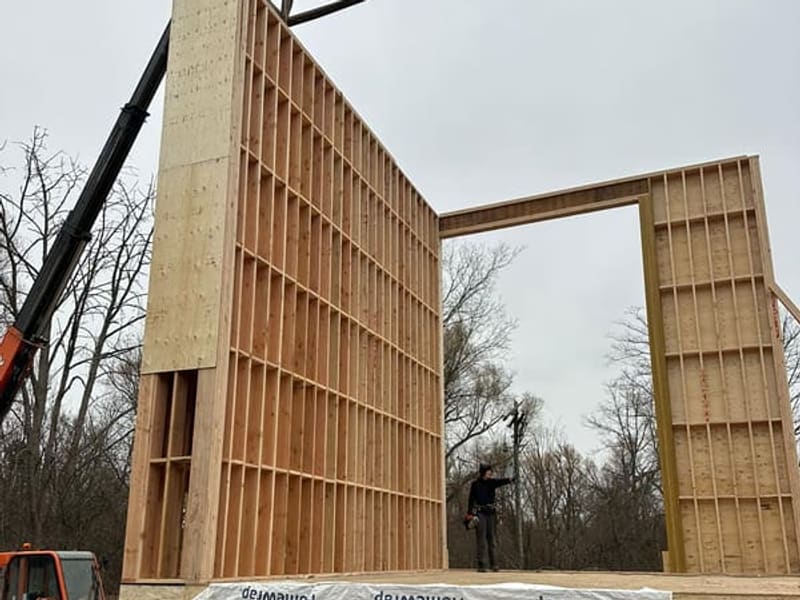 Crane-assisted wall panel tilt-up showing tall framed wall sections for custom home