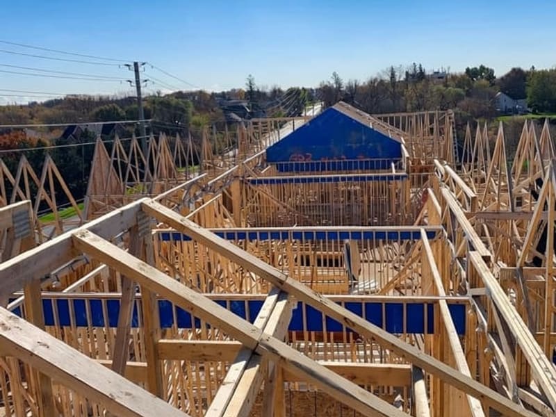 Roof truss framing viewed from above showing complex hip roof structure with blue tarps