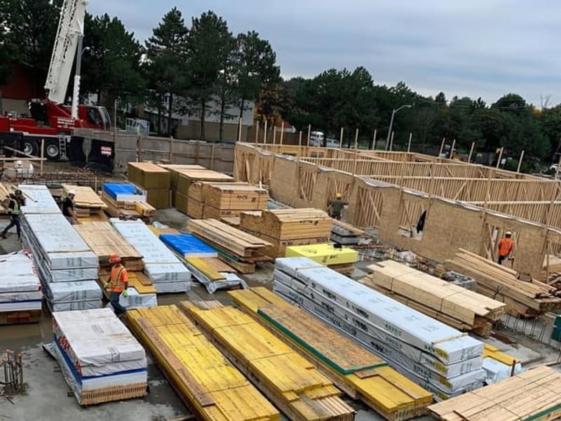 Lumber and building materials staged on site with crane and framing crew at work