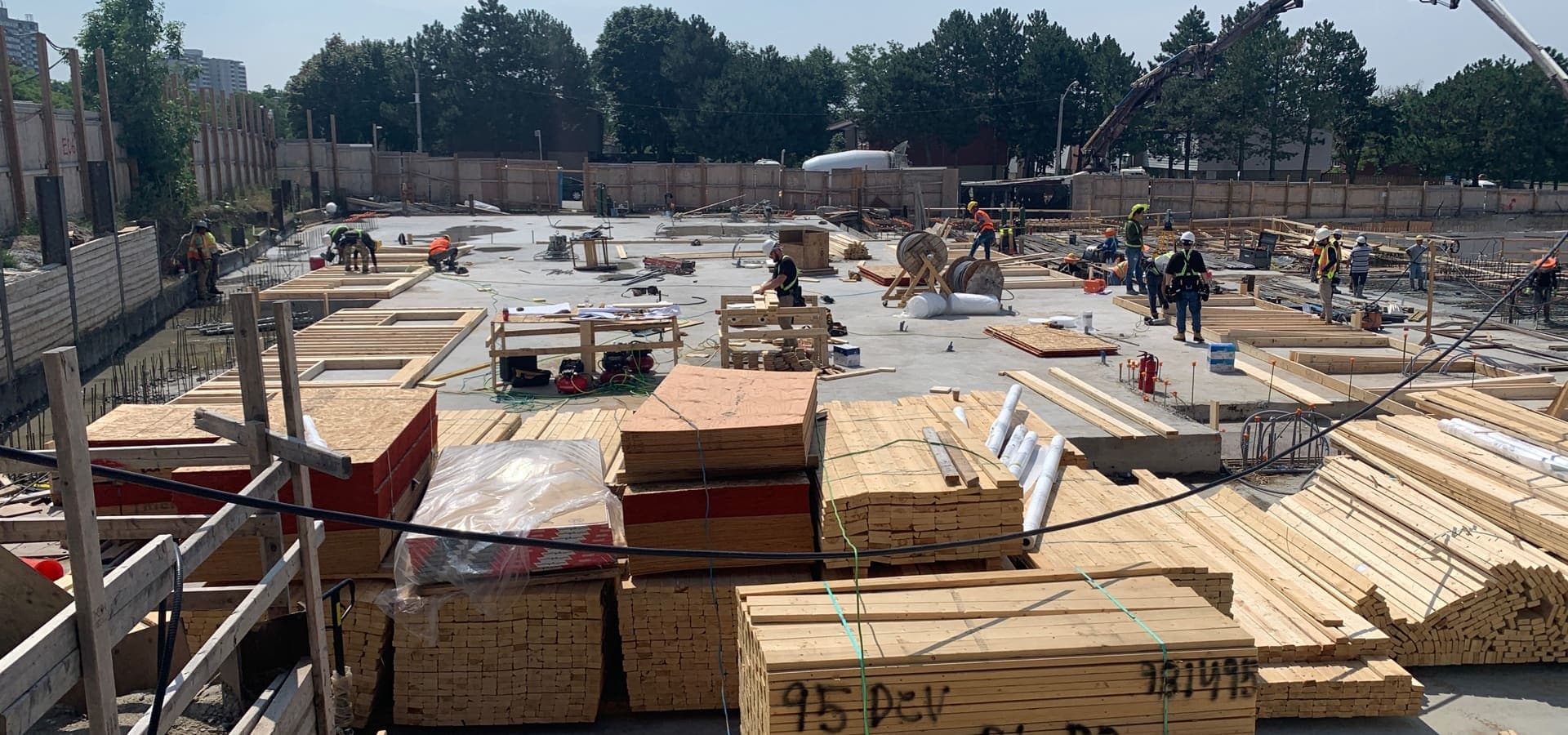 Construction site foundation with stacked lumber and workers preparing for townhome framing in Markham